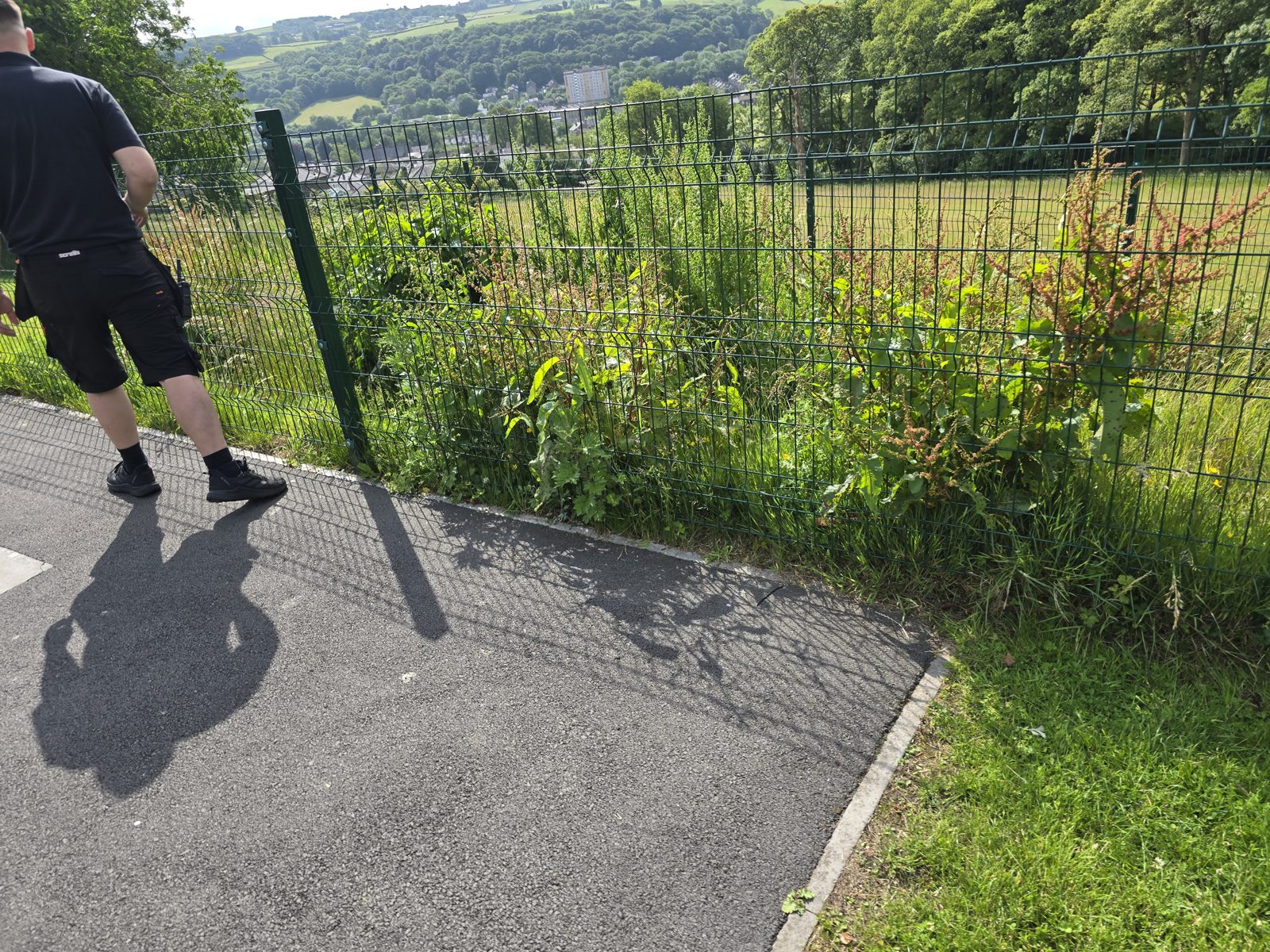 Man leaning his bodyweight into a mesh boundary fence from a tarmac path, feet braced